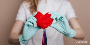 Eine Krankenschwester trägt Gummihandschuhe und hält ein Plüschherz vor sich
