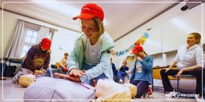 Ein Grundschulkind sitzt vor einer Reanimationspuppe und übt unter Anleitung die Herzdruckmassage.