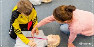 Trainerin erklärt einem Schulkind die Übungspuppe